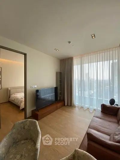 Modern living room with natural light and city view, featuring cozy seating and a flat-screen TV.