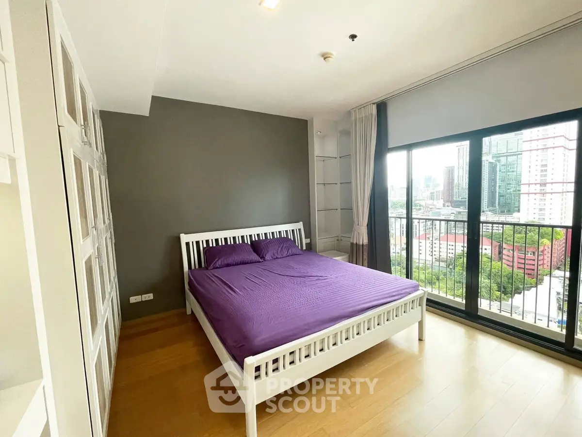 Modern bedroom with city view and large window, featuring a cozy bed and wooden flooring.