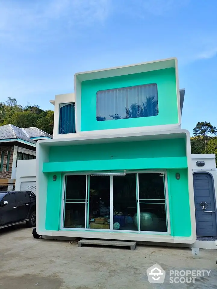 Modern two-story turquoise house with large windows and a sleek design, set against a clear blue sky.