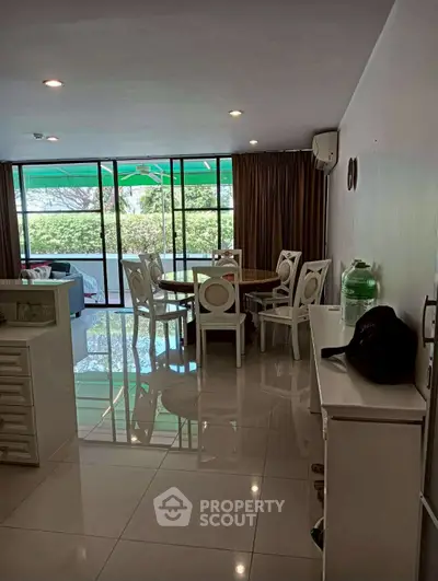 Spacious living room with dining area and large windows overlooking greenery.