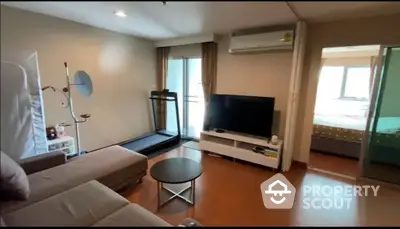 Modern living room with treadmill and TV, adjacent to a cozy bedroom.