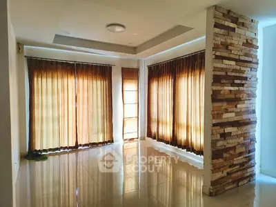 Spacious living room with large windows and stylish stone accent wall, perfect for natural light lovers.