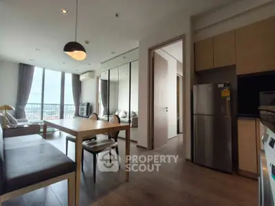 Modern open-plan living room with dining area and kitchen, featuring large windows and stylish decor.