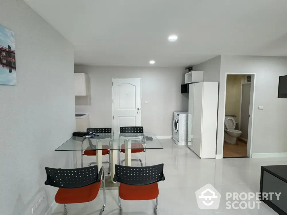 Modern apartment interior with glass dining table and washing machine in open layout.