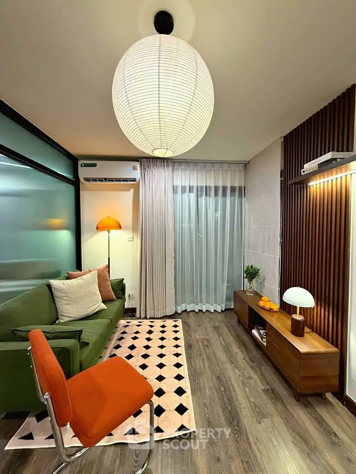 Stylish living room with modern decor, featuring a green sofa, orange chair, and elegant lighting.