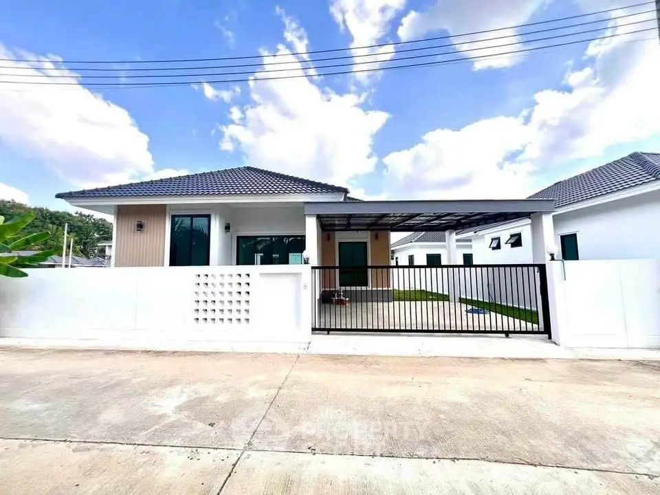 Modern single-story house with gated driveway and tiled roof under a clear blue sky.