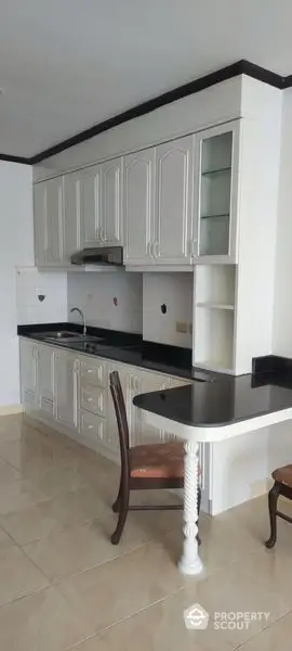 Elegant kitchen with classic white cabinetry and contrasting black countertops, featuring ample storage and a cozy breakfast nook.