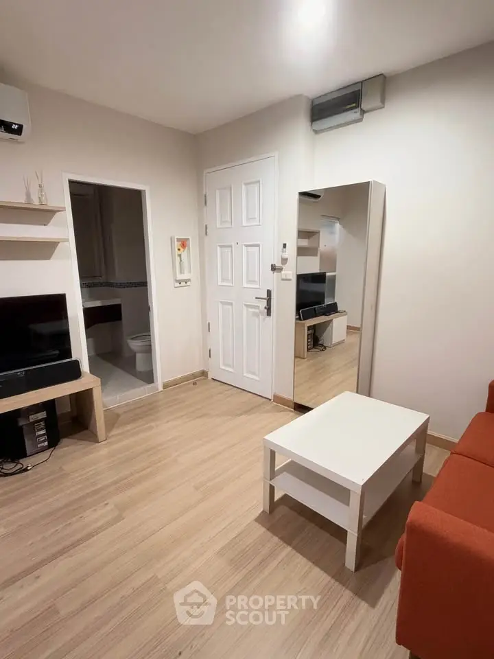 Cozy living room with modern decor and wooden flooring, featuring a sleek white door and compact furniture.