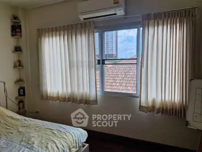 Cozy bedroom with large window and city view, featuring air conditioning and elegant curtains.
