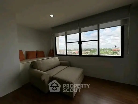 Spacious living room with large window offering stunning city views and cozy seating area.