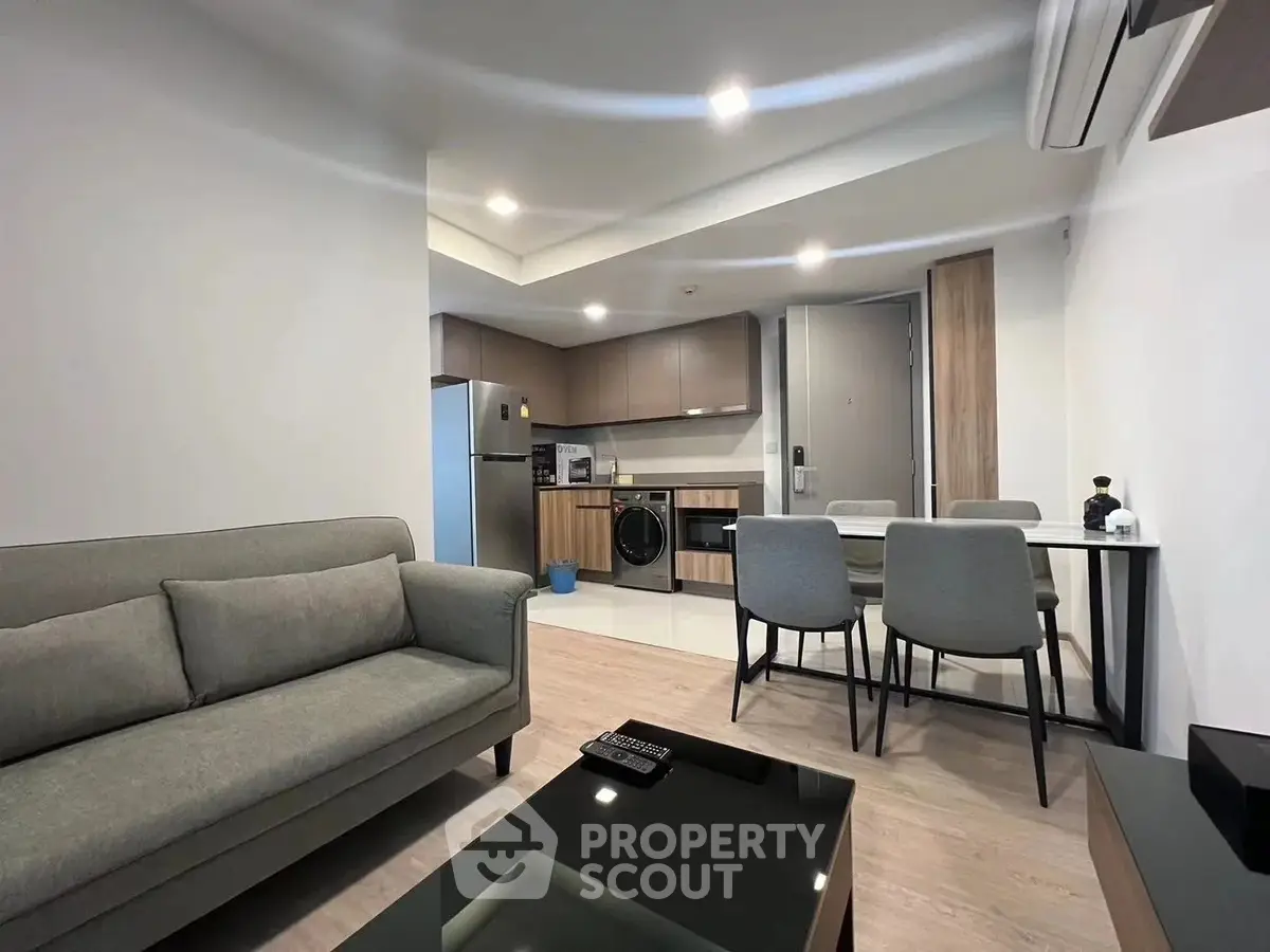 Modern living room with open kitchen, featuring sleek furniture and appliances.