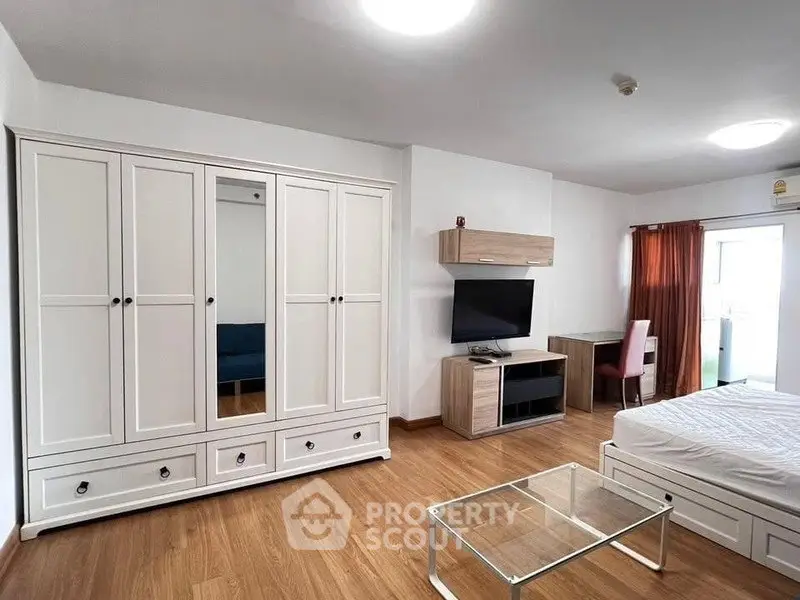 Spacious modern bedroom with wooden flooring, large wardrobe, and sleek furniture in a bright apartment.