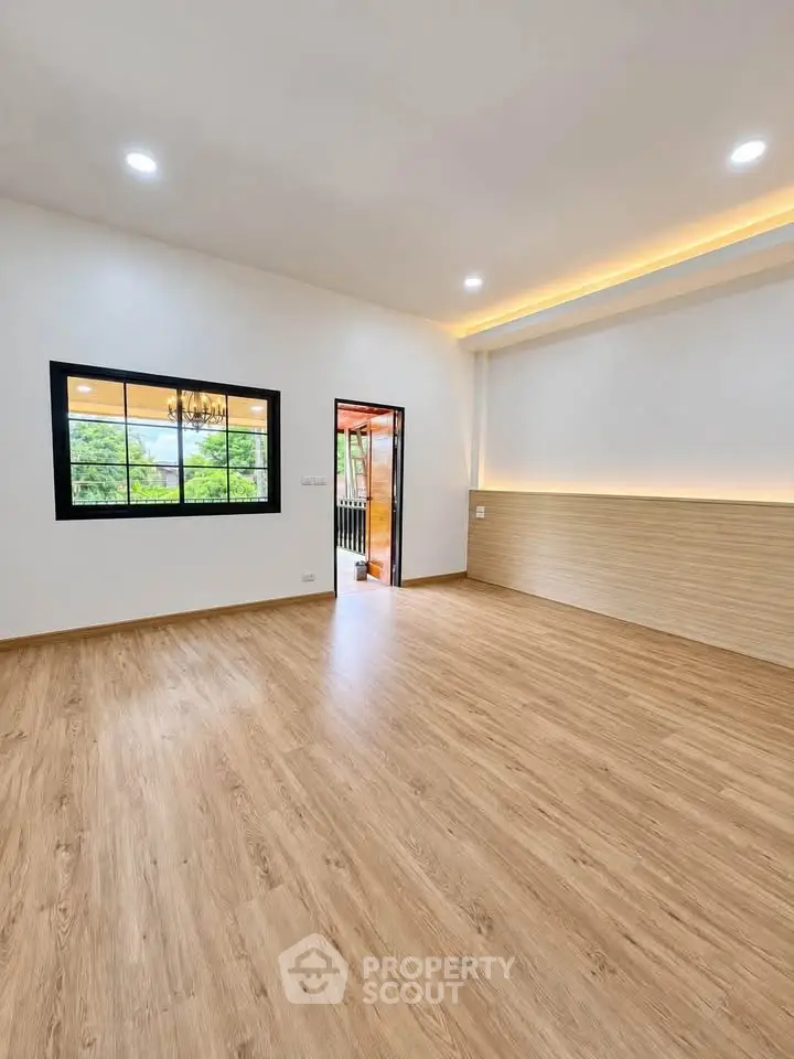Spacious modern living room with wooden flooring and large window view.