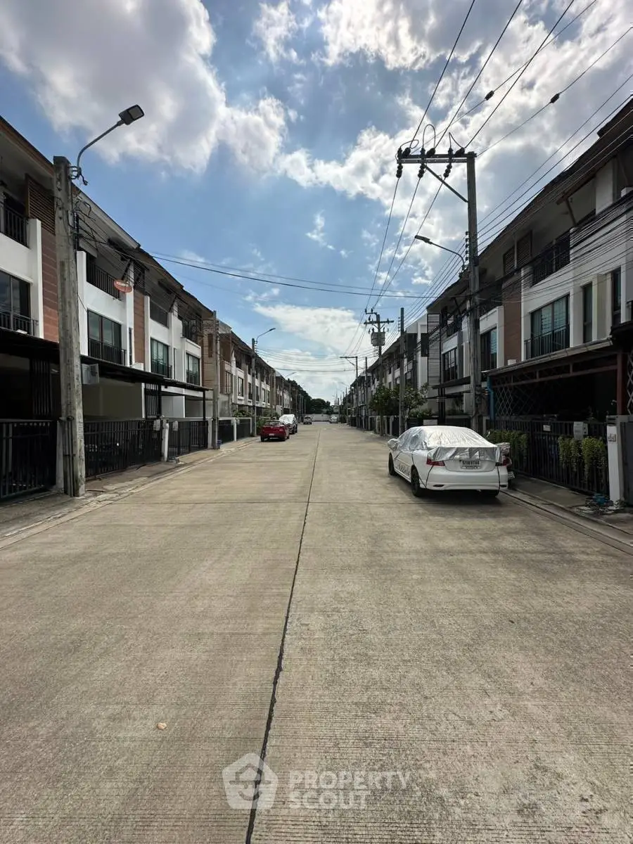 Charming residential street with modern townhouses and parked cars under a clear blue sky.