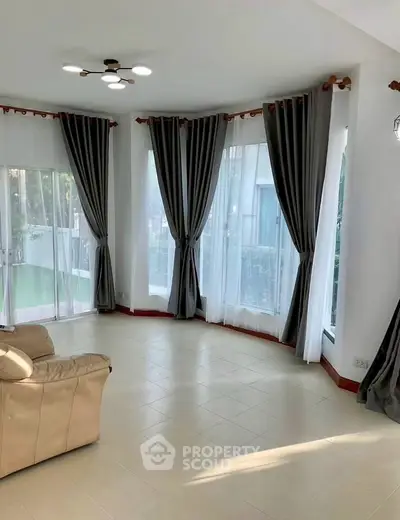 Spacious living room with large windows and elegant curtains, perfect for natural light and relaxation.