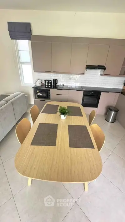 Modern kitchen with sleek cabinetry and dining area, featuring a stylish wooden table and contemporary appliances.