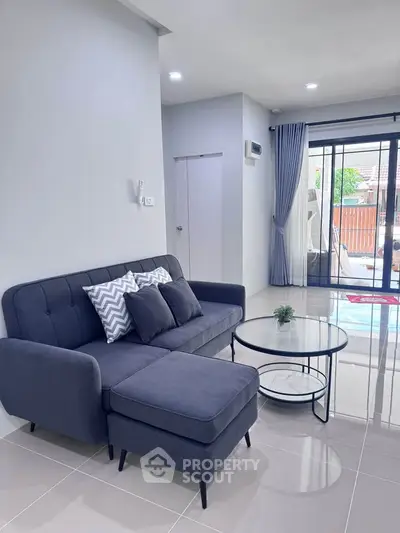 Modern living room with stylish gray sofa and glass coffee table, featuring large windows for natural light.