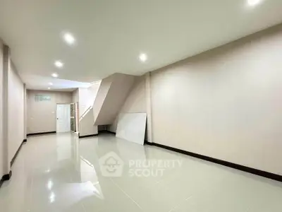 Spacious empty room with glossy tiled floor and staircase, ideal for customization.