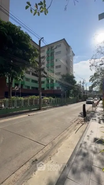Street view of residential building with clear blue sky and greenery.