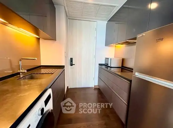 Modern kitchen with sleek cabinetry, washing machine, and stainless steel fridge in a compact layout.