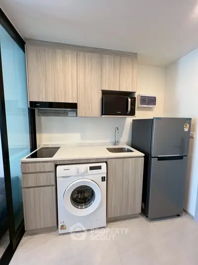 Modern compact kitchen with washing machine, microwave, and fridge in sleek design.