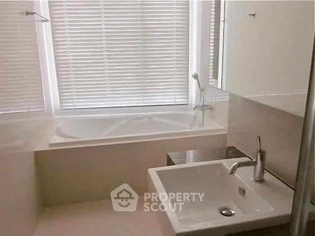 Modern bathroom with sleek sink and bathtub, featuring elegant blinds for privacy.