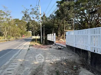 Scenic roadside view with white fence and lush greenery, ideal for real estate development.