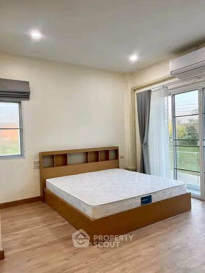 Spacious bedroom with large window and balcony access, featuring a wooden bed frame and air conditioning.