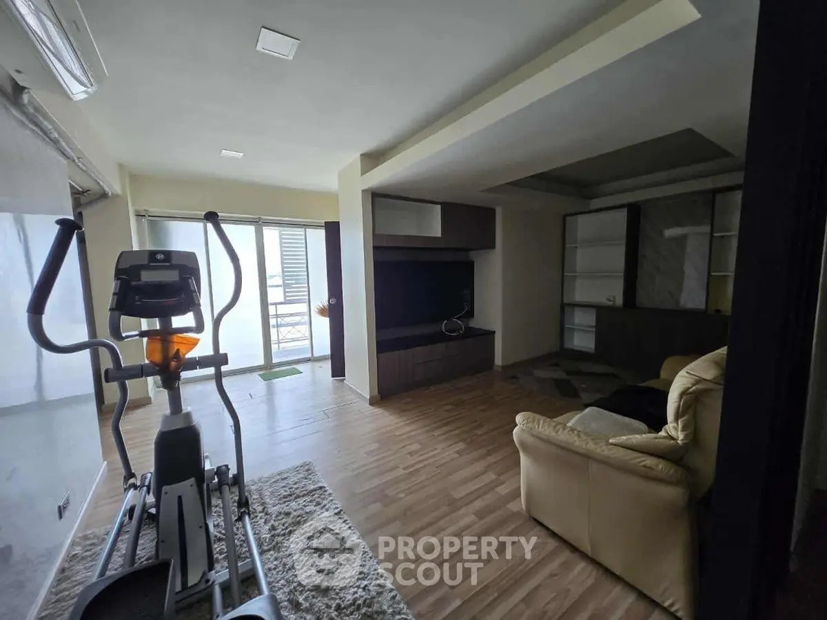 Spacious living room with exercise equipment and modern decor, featuring large windows for natural light.