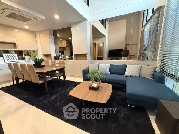 Modern living room with open kitchen, stylish furniture, and large windows for natural light.