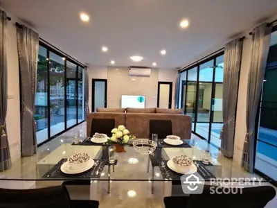 Elegant dining area seamlessly connects to a cozy living space, featuring glossy floors, modern lighting, and large windows with pool view.