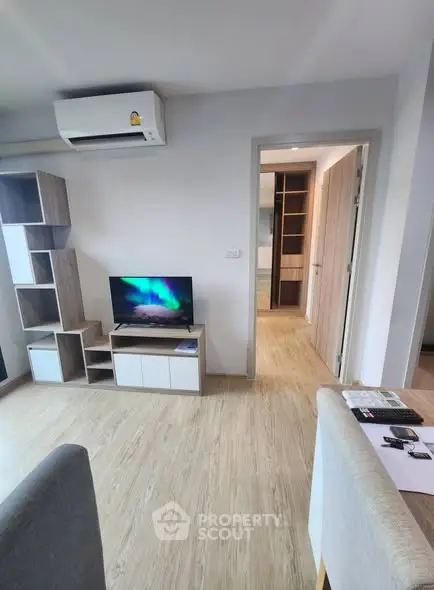 Modern living room with TV and air conditioning, featuring wooden flooring and open doorway.