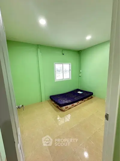 Minimalist bedroom with green walls and single mattress on tiled floor.