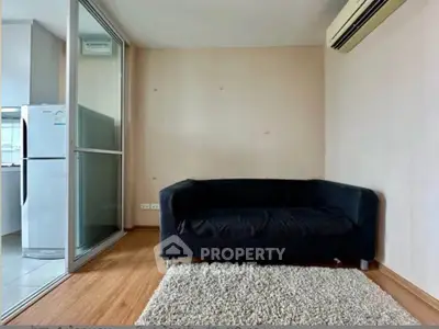 Cozy living room with modern sofa and air conditioning, adjacent to a sleek kitchen area.