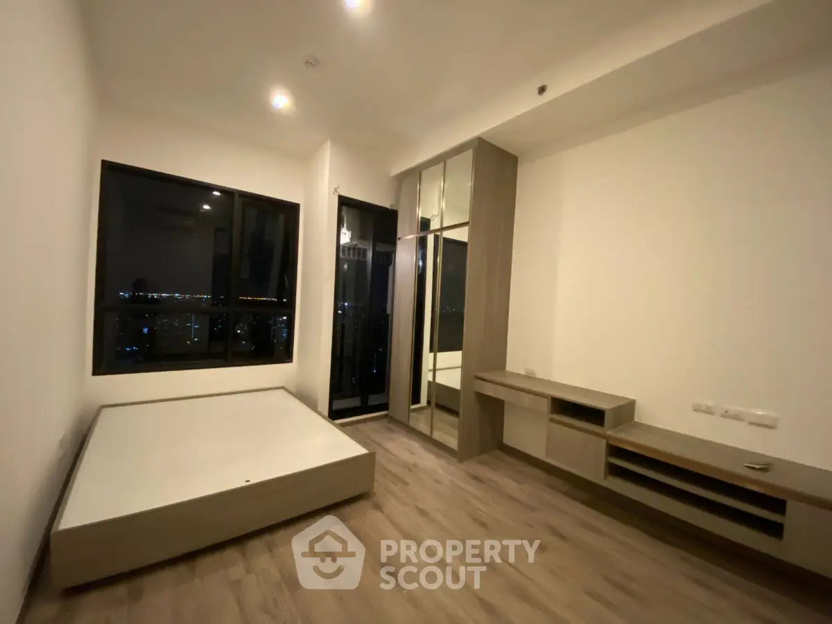 Modern bedroom with large window and built-in storage, offering city views.