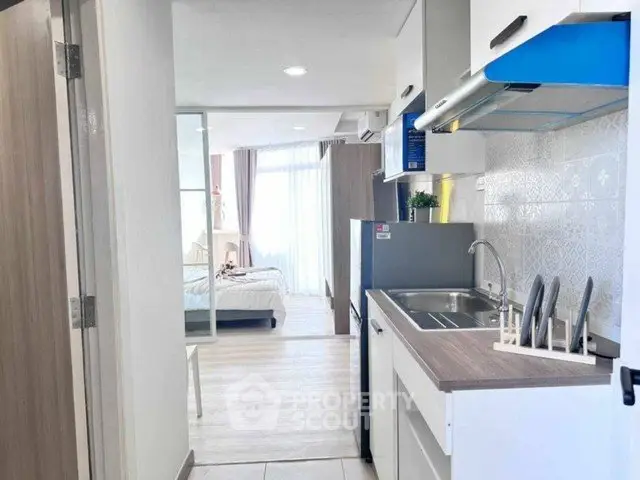 Modern compact kitchen with open layout leading to a bright bedroom with large windows.