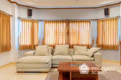 Spacious and inviting living room with plush cream sofas, elegant golden drapes, and warm ambient lighting, perfect for relaxation and entertaining guests.