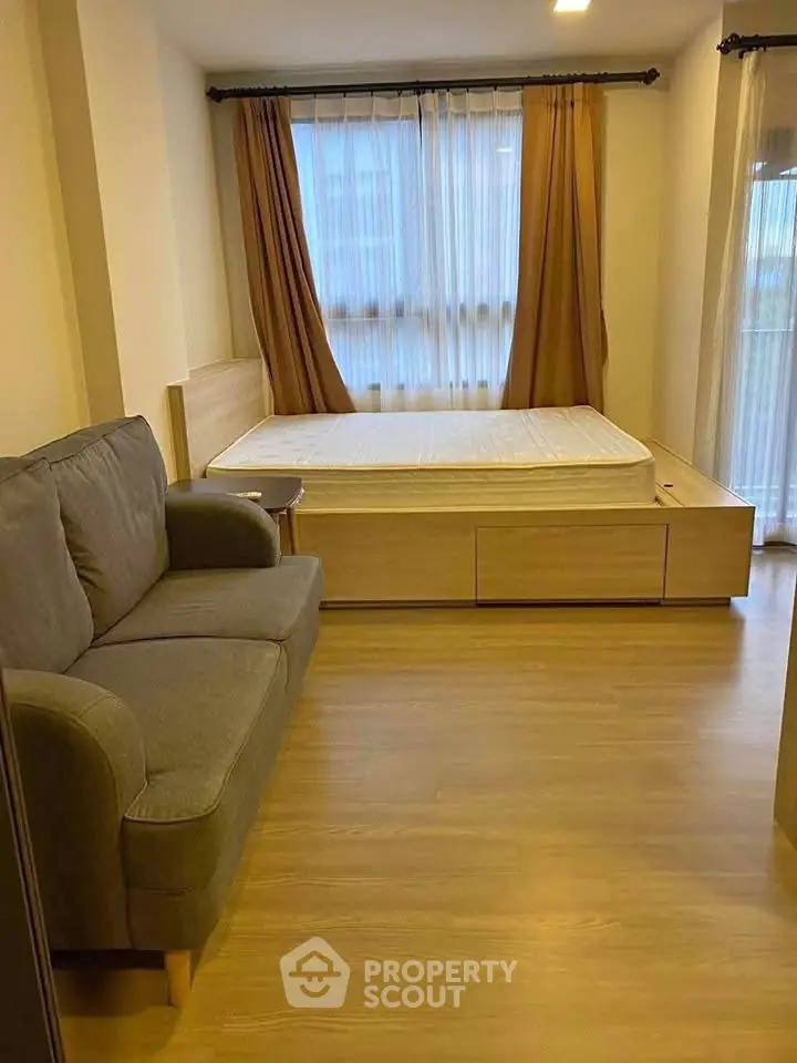 Cozy bedroom with wooden flooring, bed, and sofa, featuring large windows with curtains.