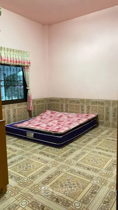 Cozy bedroom with tiled floor and window view, featuring a simple mattress setup.