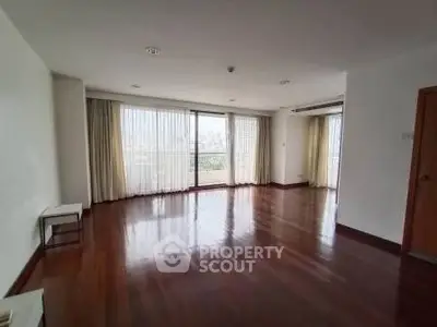 Spacious living room with hardwood floors and large windows offering natural light and city views.