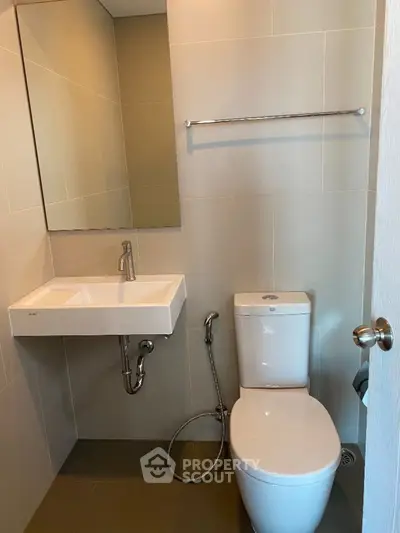 Modern bathroom with sleek fixtures and neutral tiles, featuring a wall-mounted sink and toilet.