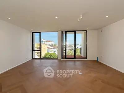 Spacious living room with large windows and balcony access, offering stunning city views.