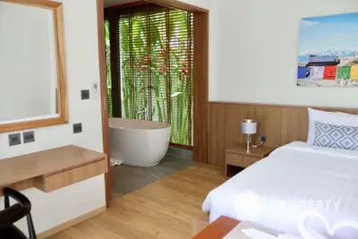 Spacious bedroom with modern design, featuring a freestanding bathtub, hardwood floors, and a serene garden view through floor-to-ceiling windows.