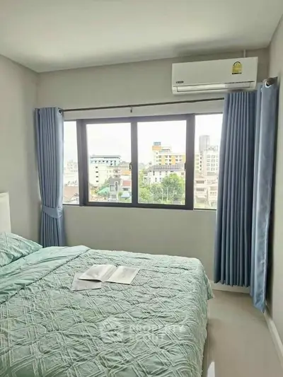 Bright bedroom with large window offering city view, featuring modern decor and air conditioning.