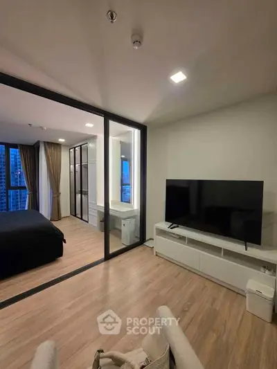 Modern living room with sleek TV setup and glass partition leading to bedroom with city view.
