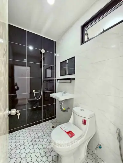 Modern bathroom with sleek black and white tiles, featuring a shower and contemporary fixtures.