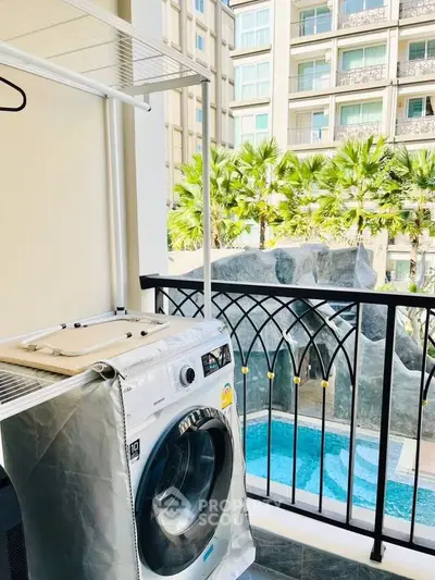 Chic balcony with washing machine overlooking a lush garden and pool in a modern apartment complex.