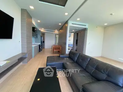 Spacious modern living room with sleek black leather sofa and open kitchen layout.