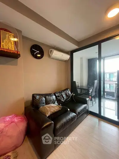Modern living room with leather sofa and glass sliding doors leading to a balcony.