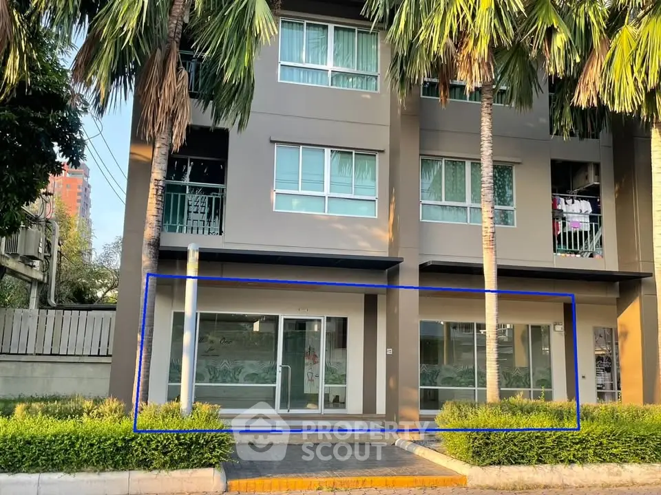 Modern apartment building exterior with palm trees and large windows, showcasing urban living.